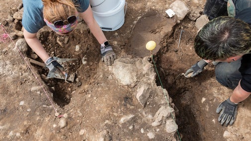 Volunteers kneeling over a dig site